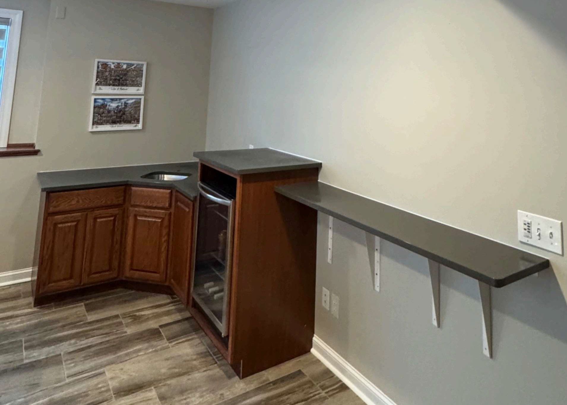 Empty kitchen corner with wood cabinets, black countertop, and a wall-mounted shelf above carpet flooring