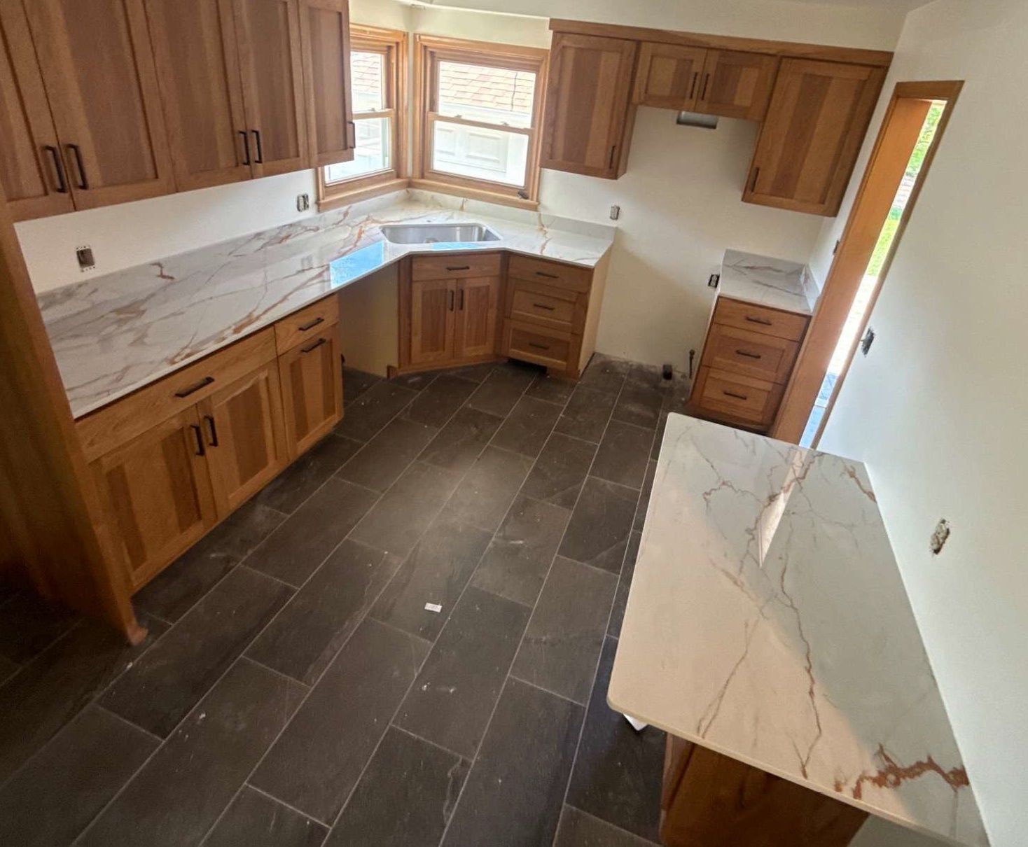 Empty kitchen with wood cabinets, dark tile floor, and marble countertops under a window