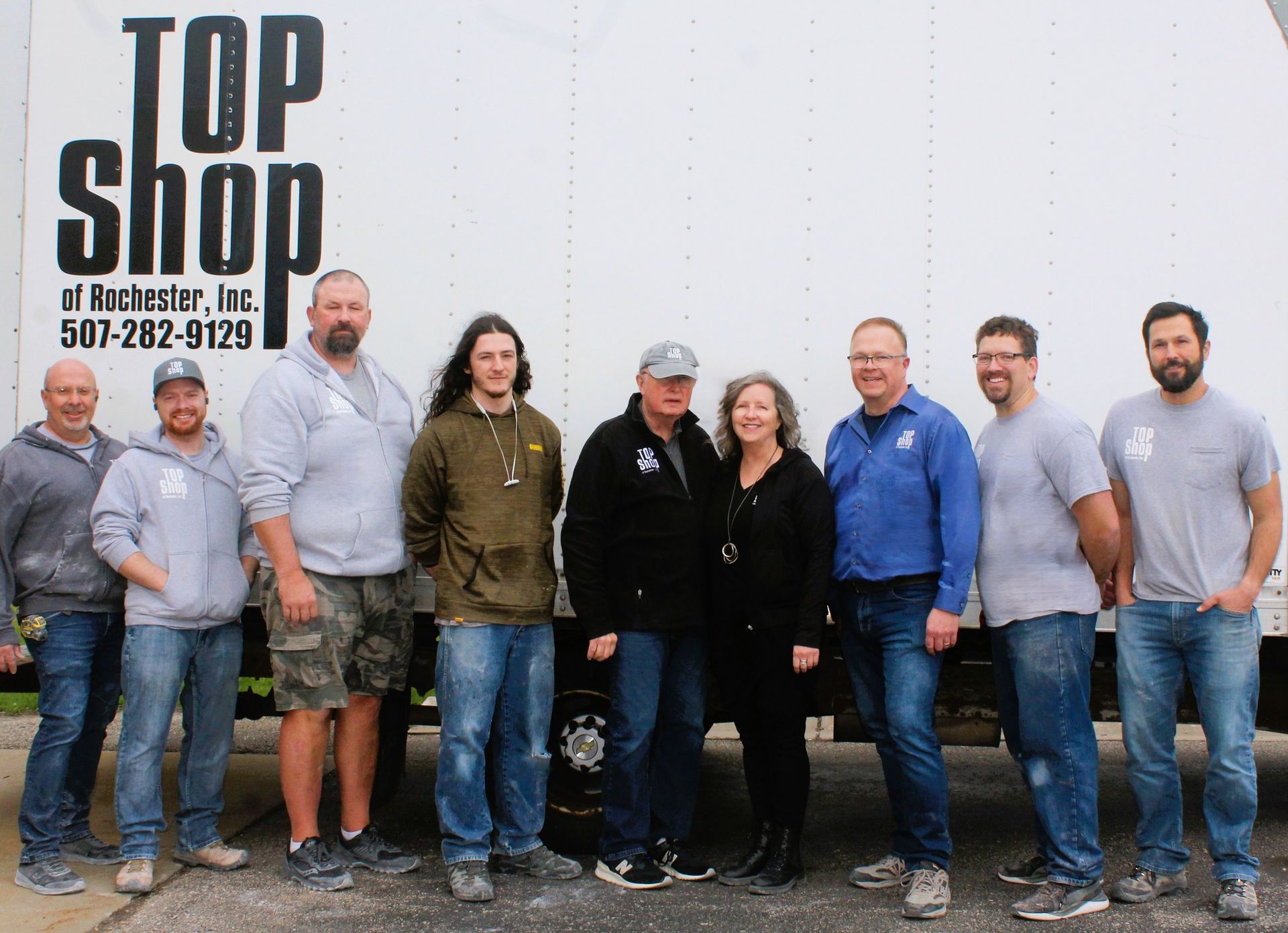 Group of people standing in front of a white truck. The truck has TOP SHOP and a phone number on it.