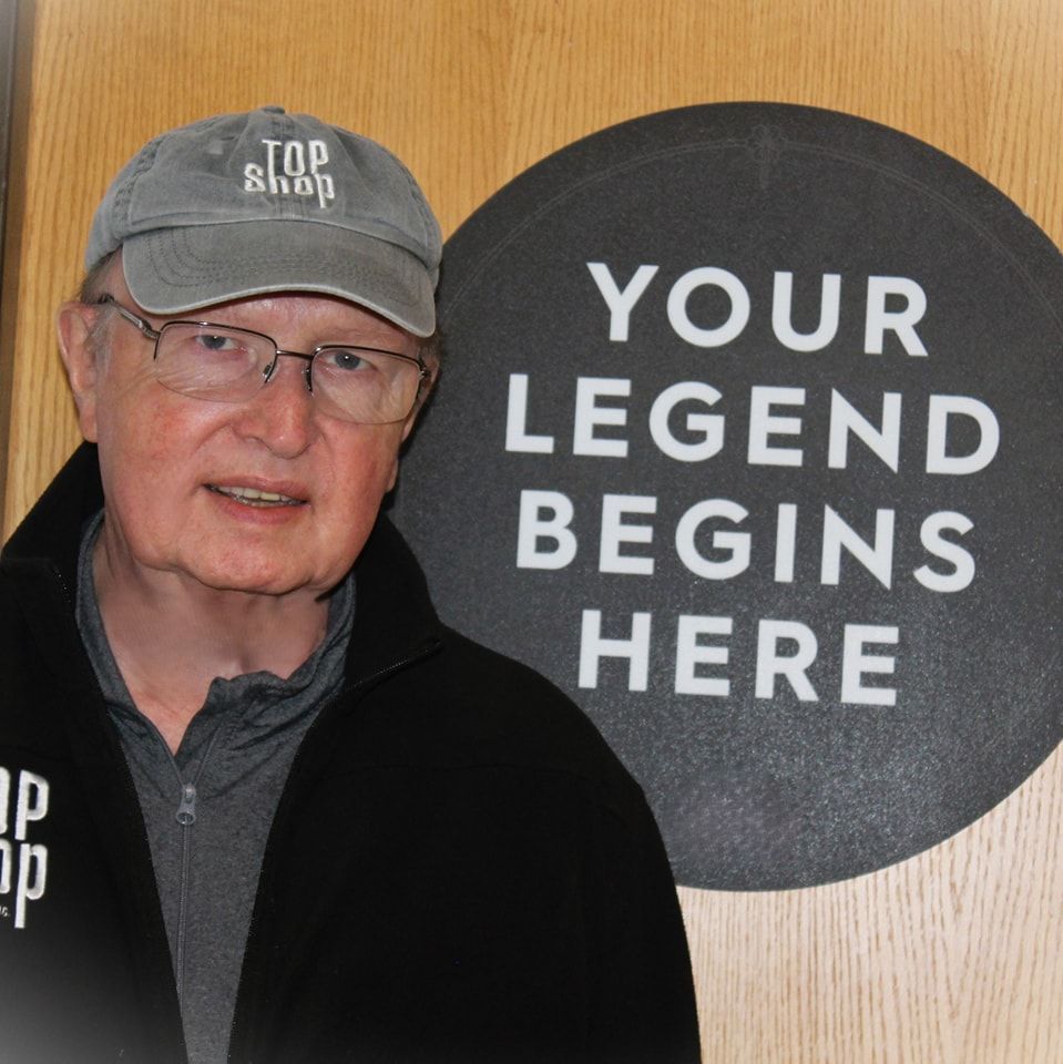 Man wearing a gray Top Shop cap and jacket, standing near a sign that reads Your Legend Begins Here.