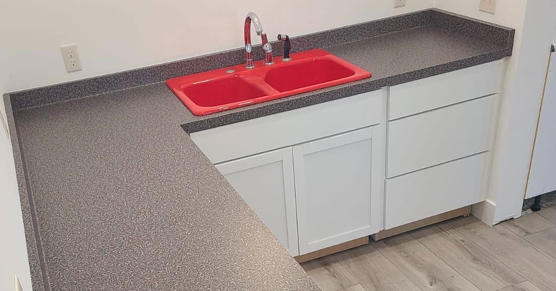 Kitchen countertop with red sink, white cabinets, and gray speckled countertop.