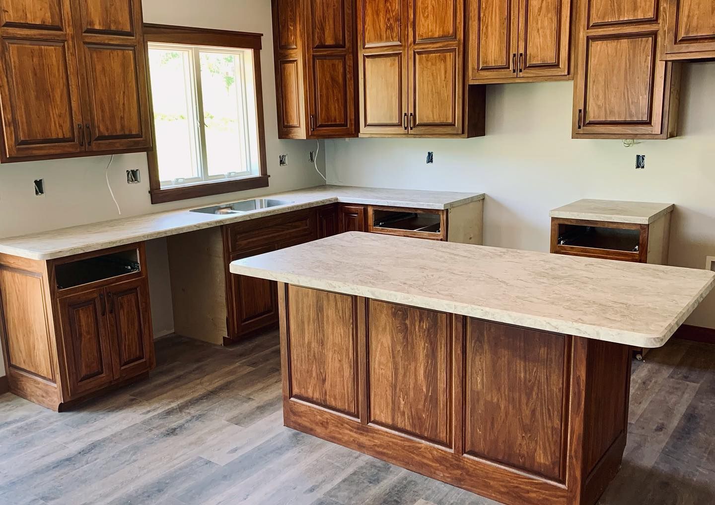 Kitchen with dark wood cabinets, light countertops, and island. Light gray wood-look floor, window, and empty wall space.