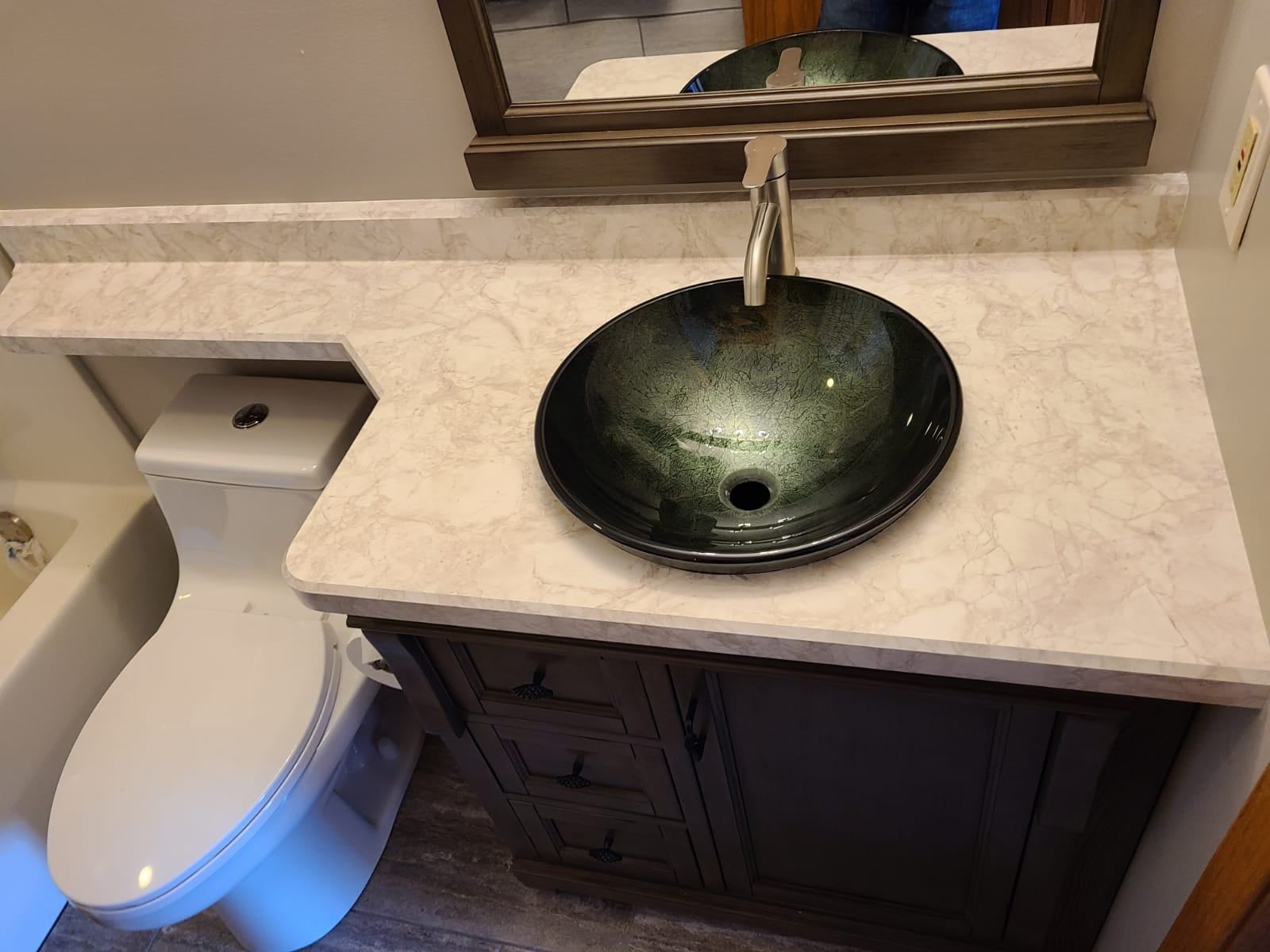 Bathroom vanity with dark brown cabinet, marble countertop, glass bowl sink, and toilet.