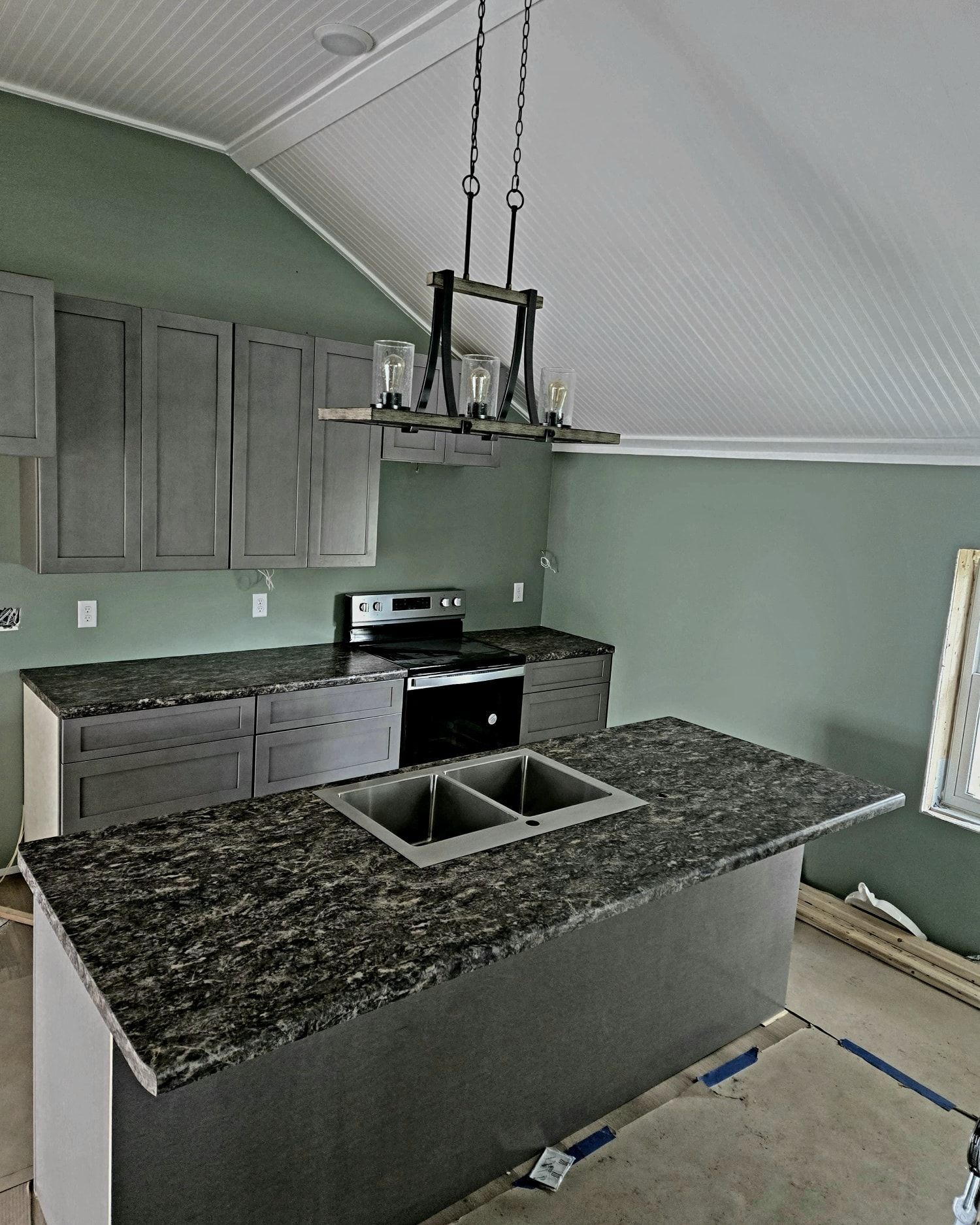 Newly constructed kitchen with grey cabinets, granite countertops, and island with sink.