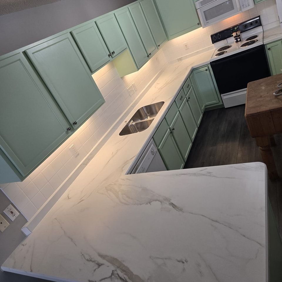 Kitchen with pale green cabinets, white countertops, and stainless steel appliances.