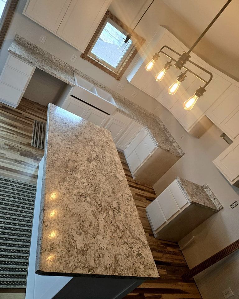 High-angle view of a modern kitchen with a large island and white cabinets. Brown granite countertops and wooden flooring.