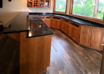 Bar with black countertop, wooden cabinets, and a window overlooking greenery.