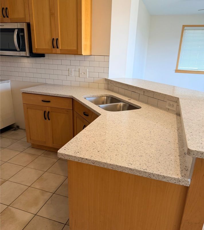 Kitchen with light-colored cabinets, white countertops, and a double sink. Tile backsplash and beige tile floor.