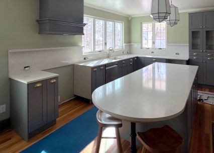 Gray kitchen with white countertops and island, wood floor, blue rug, and light green walls.