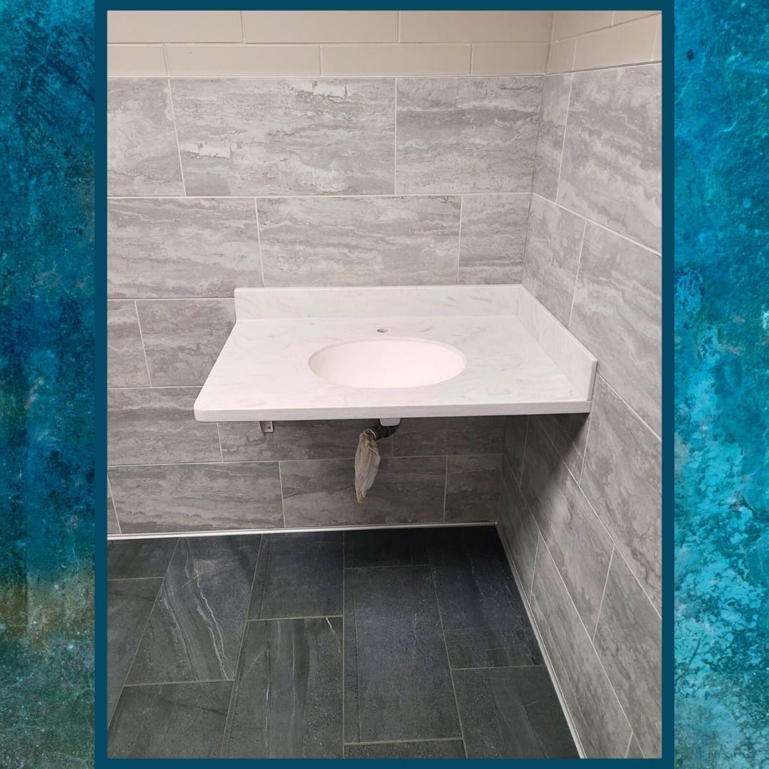 White sink installed on a gray tiled wall in a restroom. Dark tiled floor below.