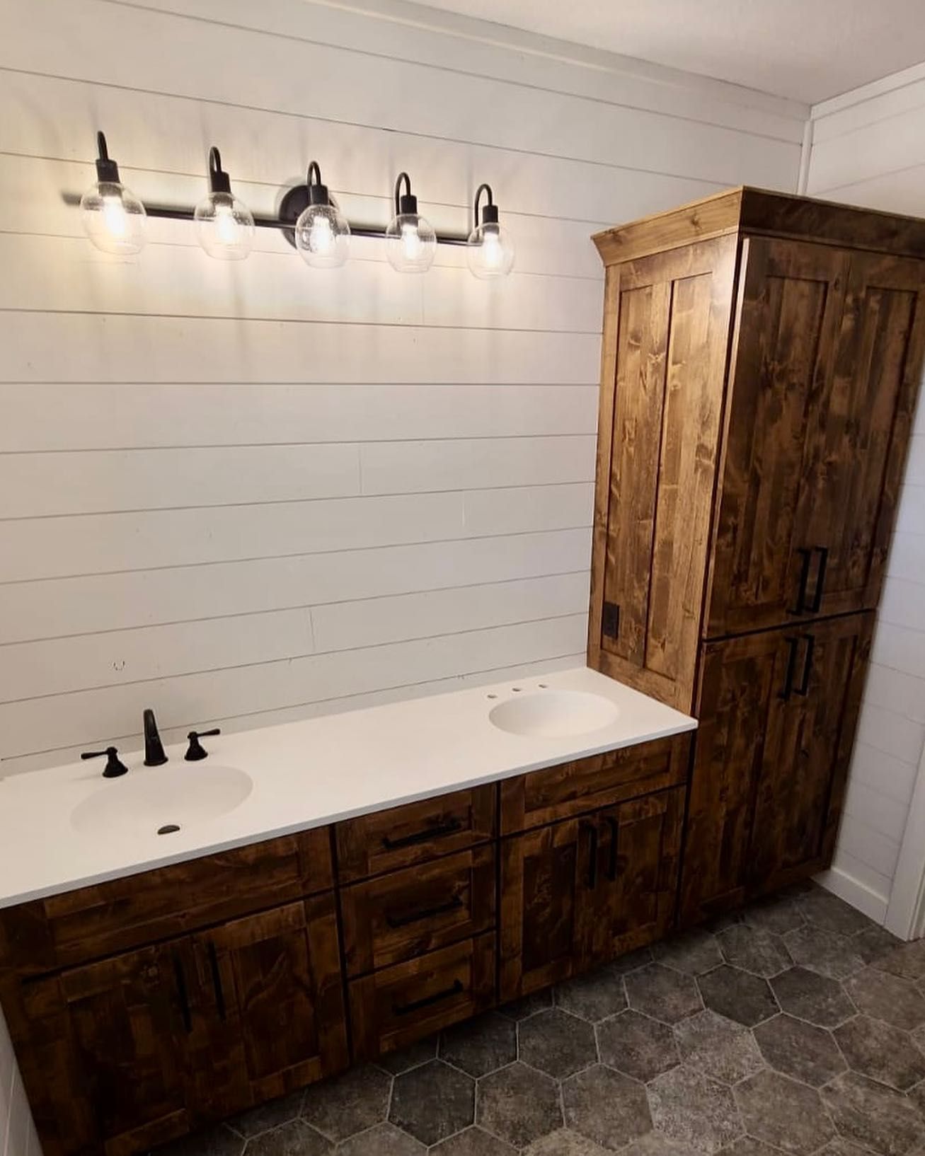 Bathroom with wood vanity and linen cabinet, white countertop, white shiplap walls, and hexagon tile floor.