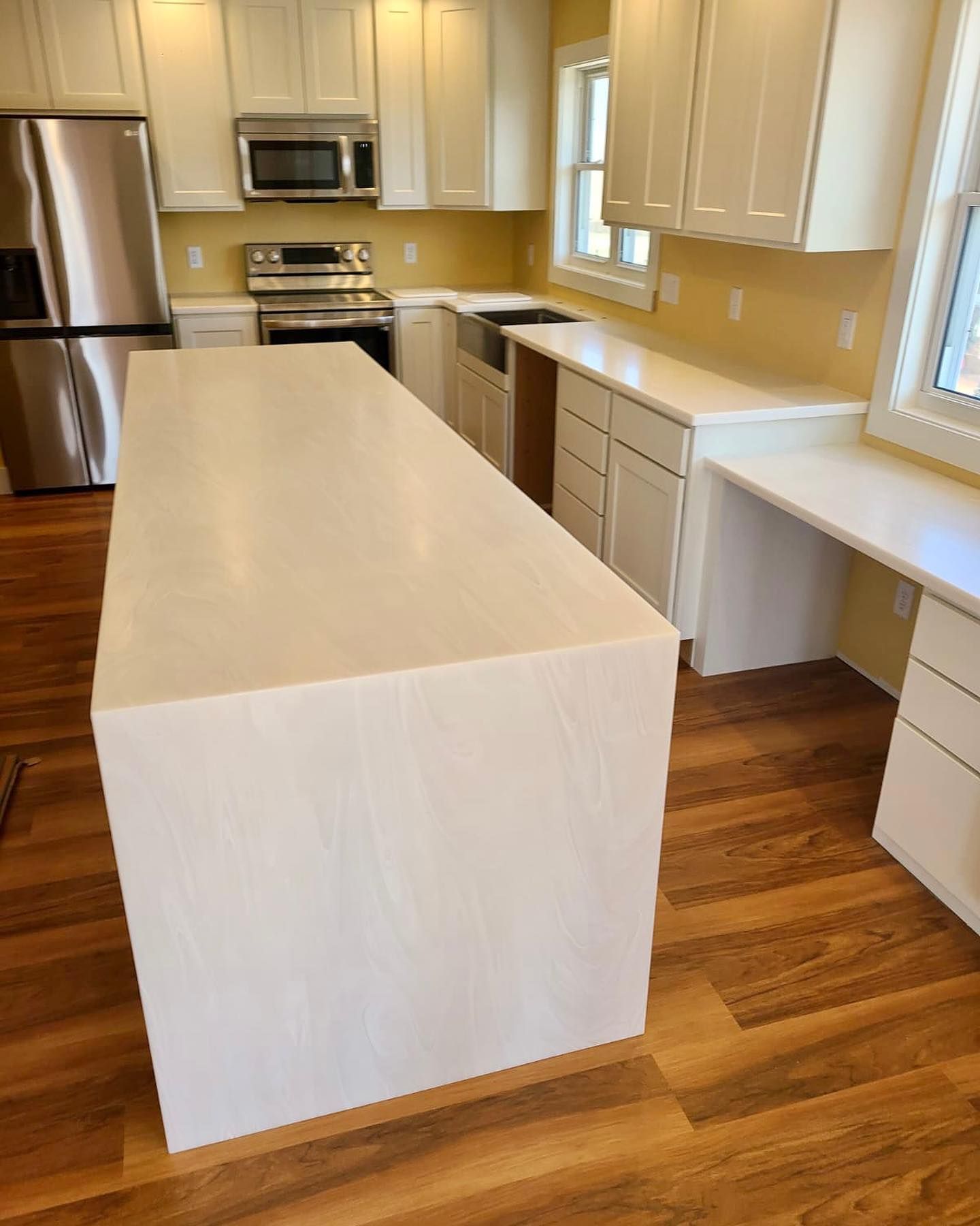 Modern kitchen with a large white island, white cabinets, stainless steel appliances, and wood-look flooring.