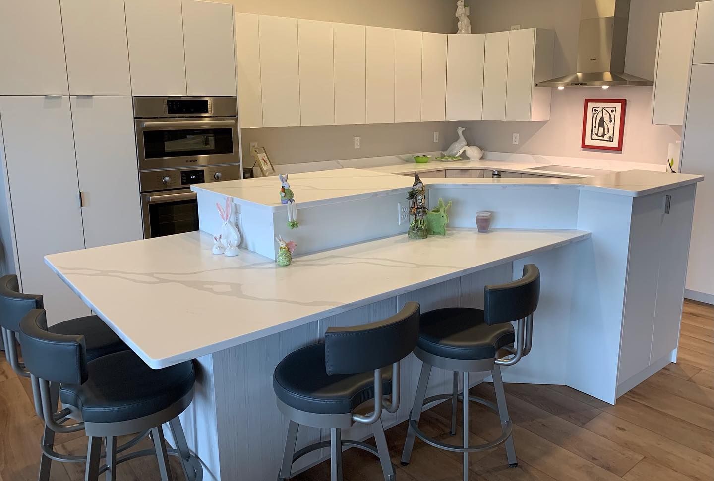 White kitchen with island and stools, built-in oven, stainless hood, and overhead cabinets.