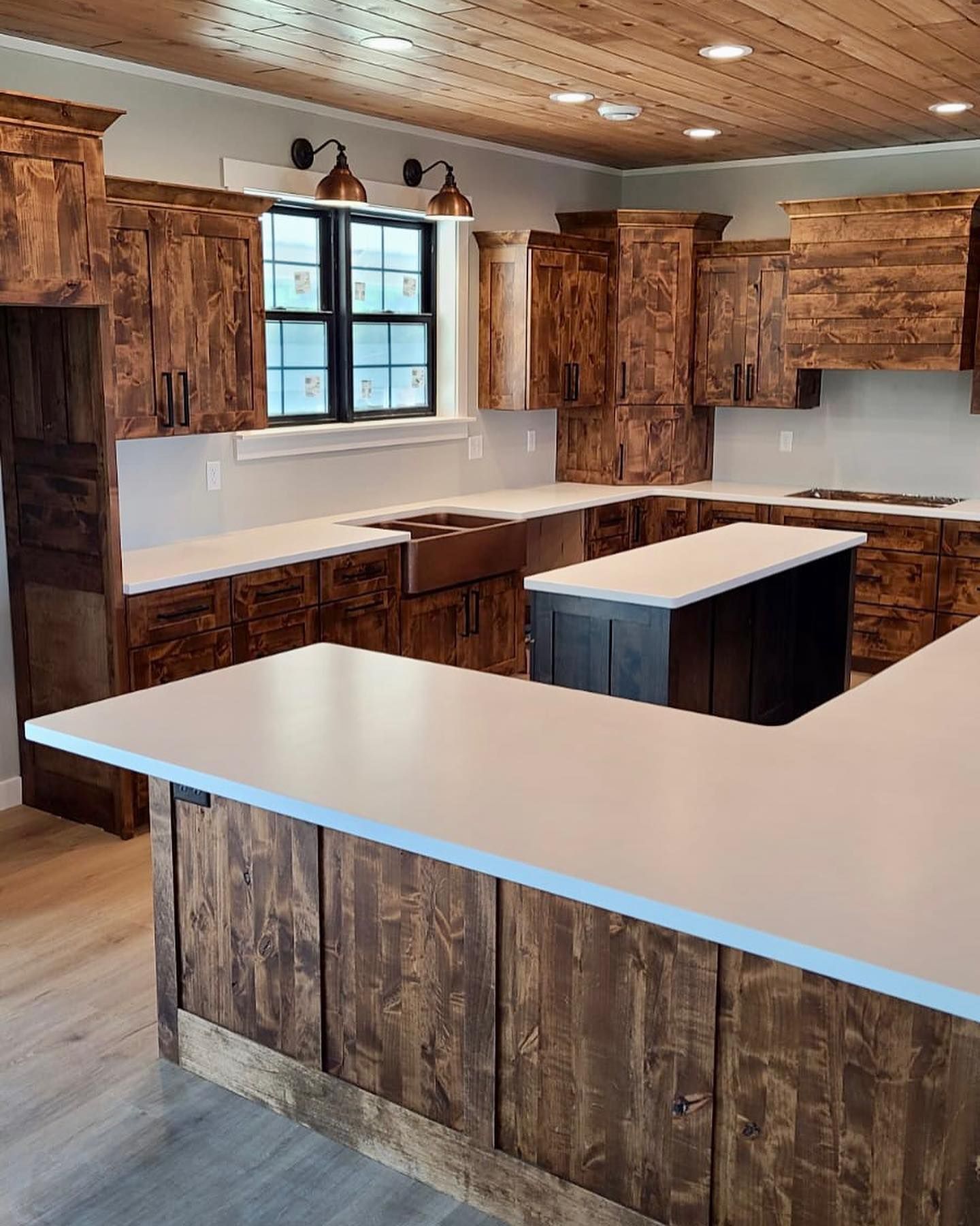 Rustic kitchen with wooden cabinets, white countertops, and a dark island.
