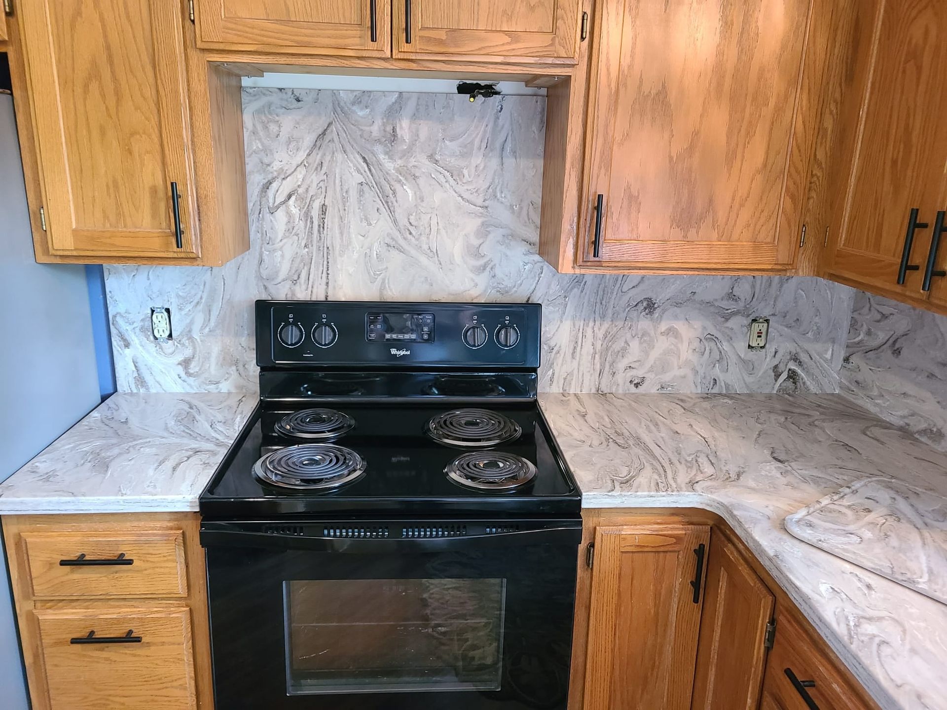 Kitchen with oak cabinets, black stove, and marble-look backsplash and countertops.