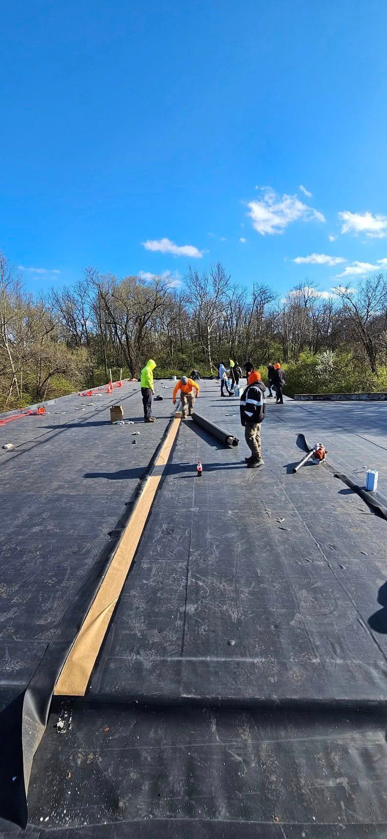Roadwork crew on a rural road under a bright blue sky, with orange cones and barrels lining the lane