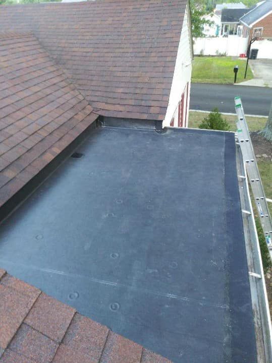 Flat black roof section beside brown shingles on a house, viewed from above.