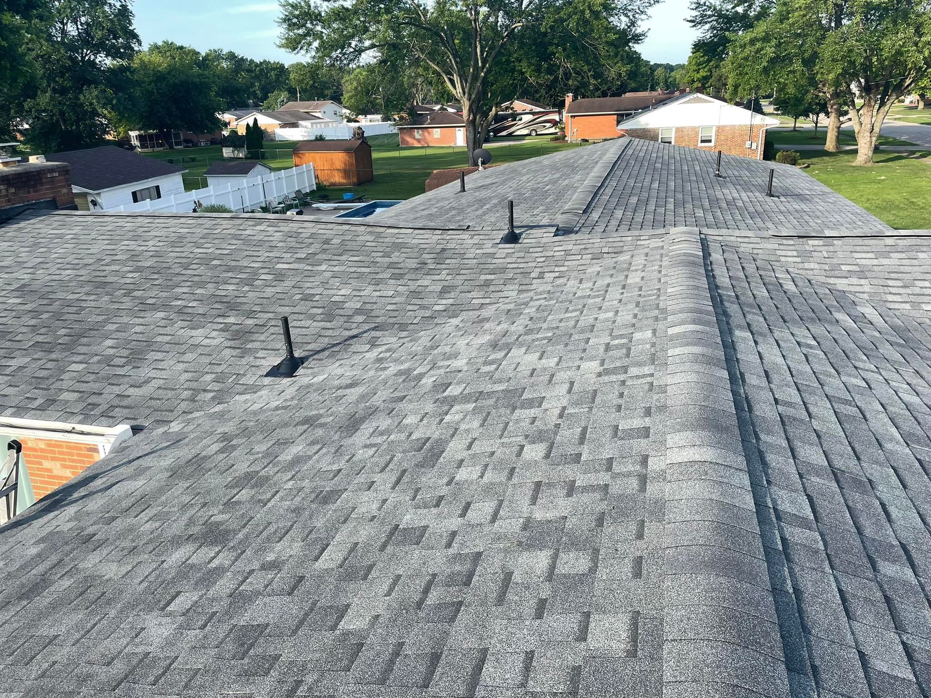 Gray shingle roof on a house, viewed from above with trees and neighboring homes in the background
