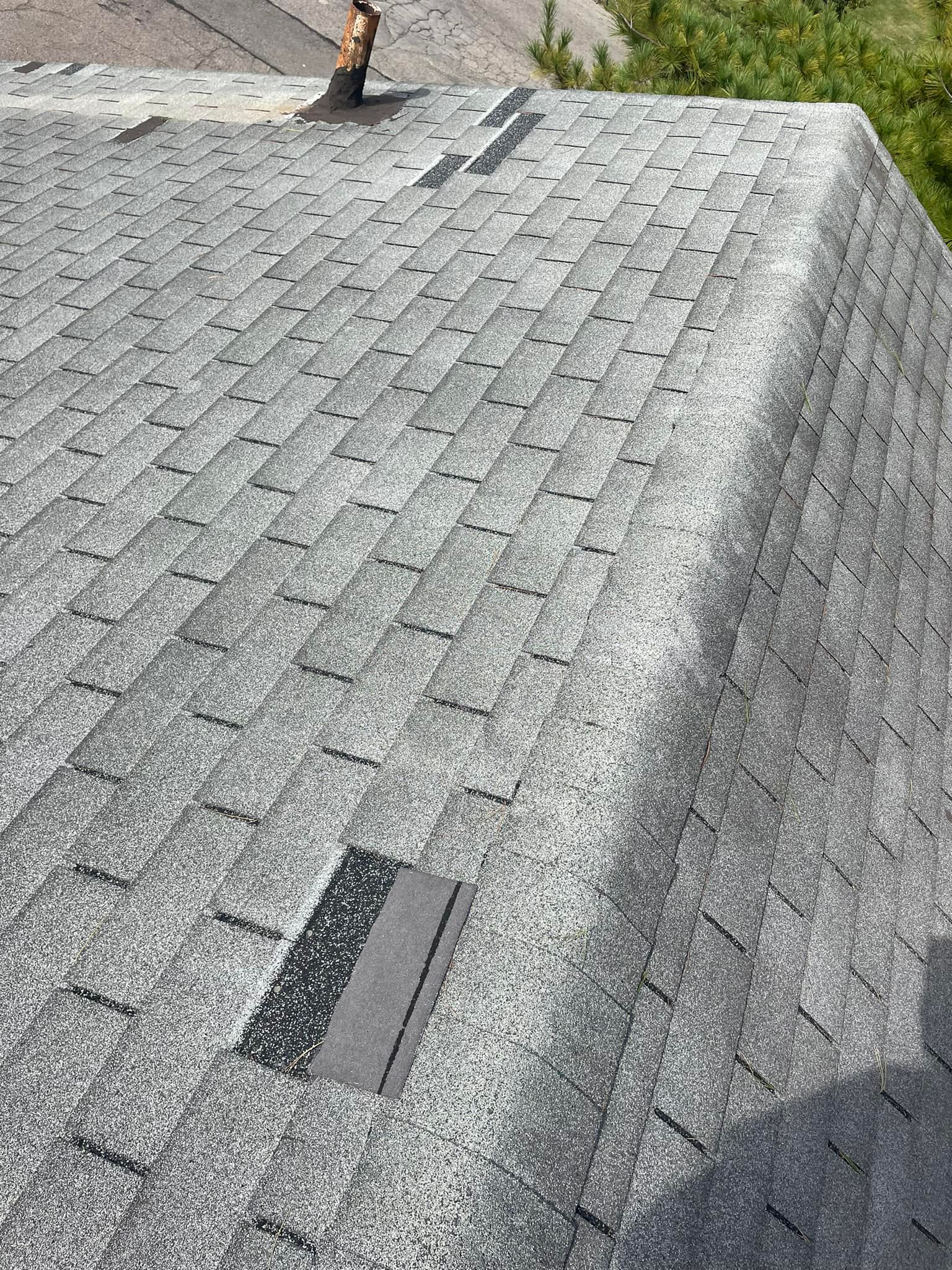 Close-up of a gray shingled roof with two dark roof vents and a shadow on the right side