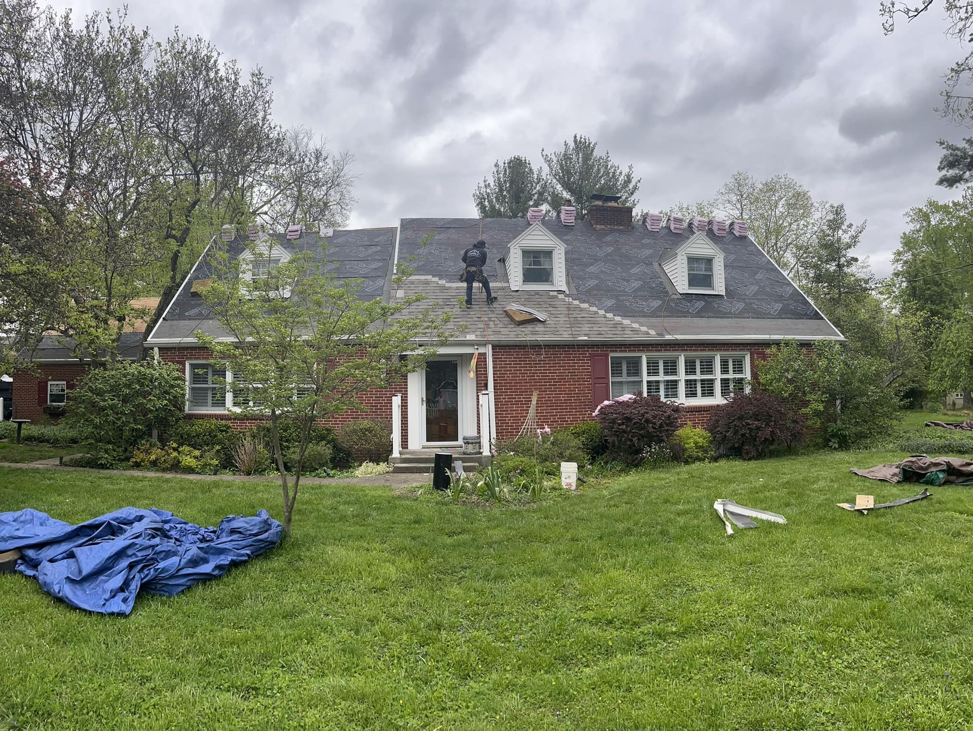 Brick house with gray roof and white trim, seen from a grassy yard with a blue tarp in front.