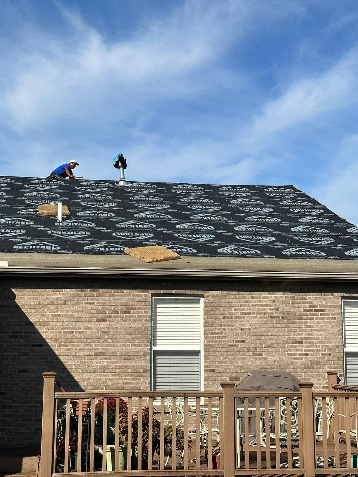 Workers on a roof repairing shingles on a brick house under a blue sky
