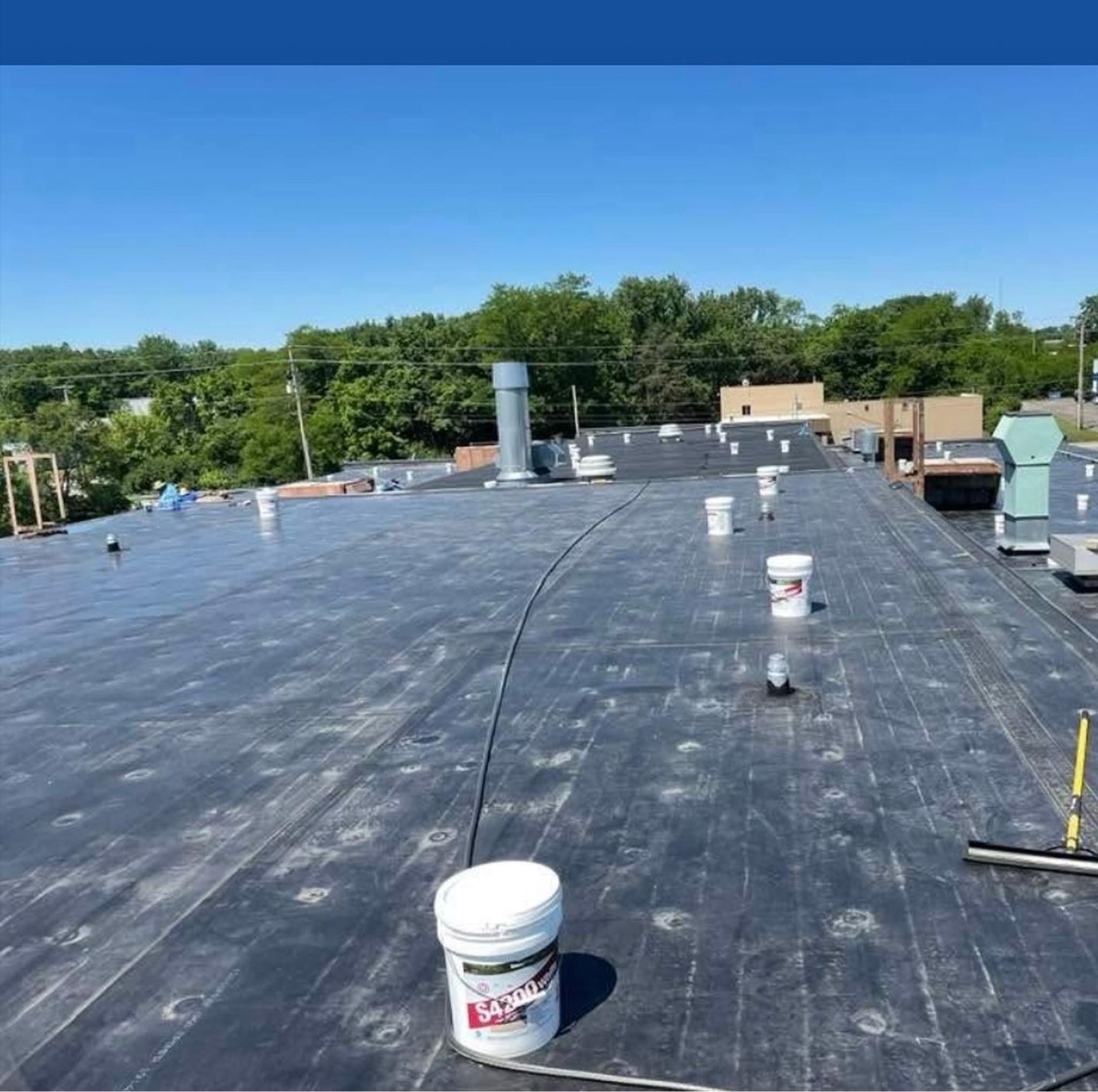 Flat rooftop with black roofing membrane, paint buckets, and HVAC vents under a clear blue sky