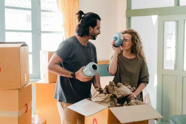 Couple unpacking a box, examining vases, smiling, indoors with cardboard boxes.