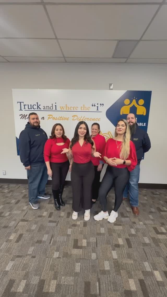 Group of six people posing in front of a company sign. They wear red shirts and black pants.