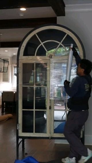 Person installing film on a tall, arched window in a home.
