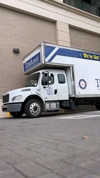 White moving truck parked next to a brick building. Truck has 