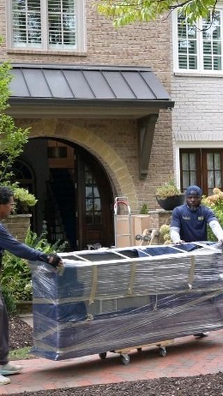 Movers carrying wrapped furniture toward a house entrance.