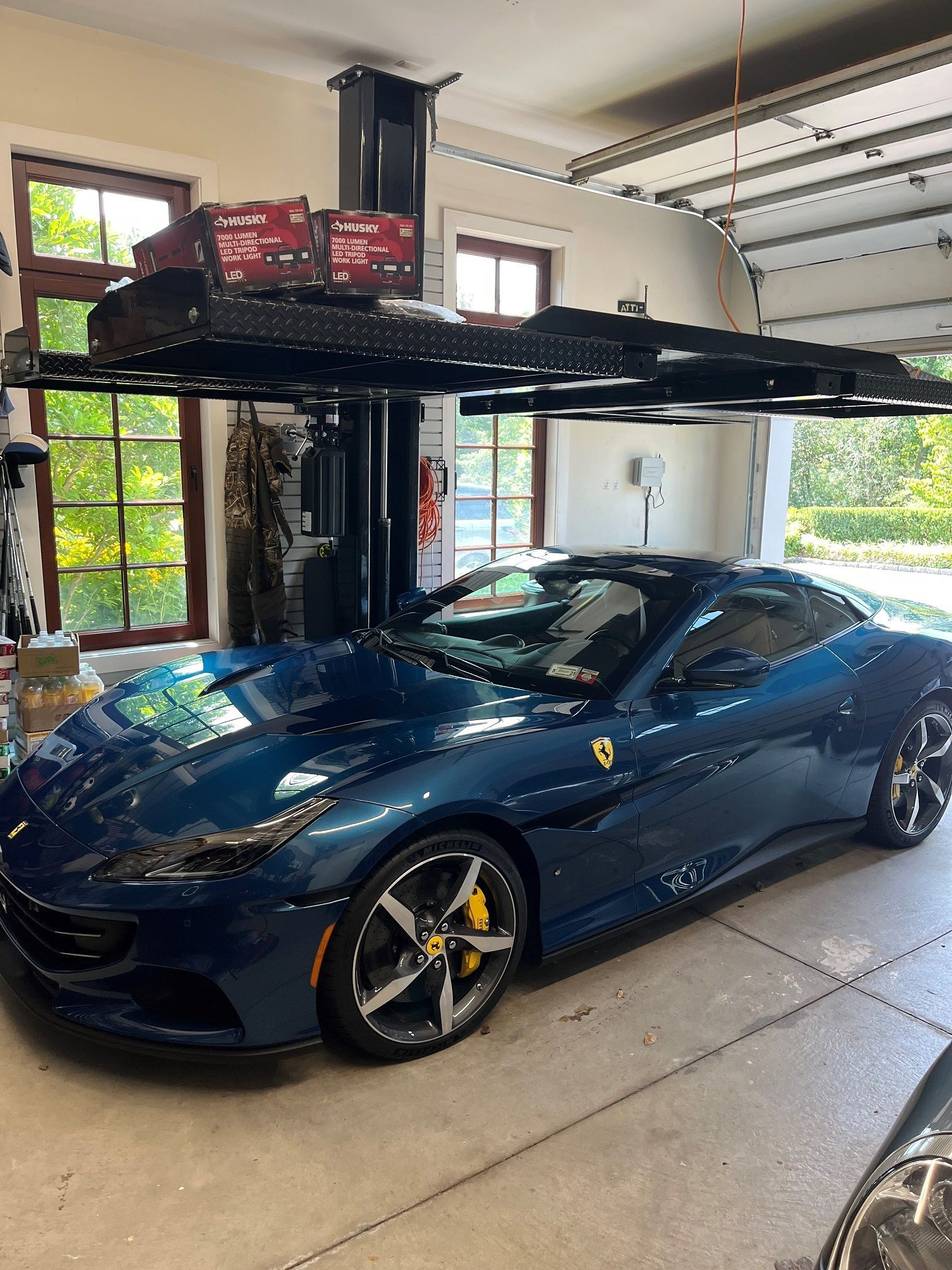 A blue ferrari is parked in a garage under a car lift.