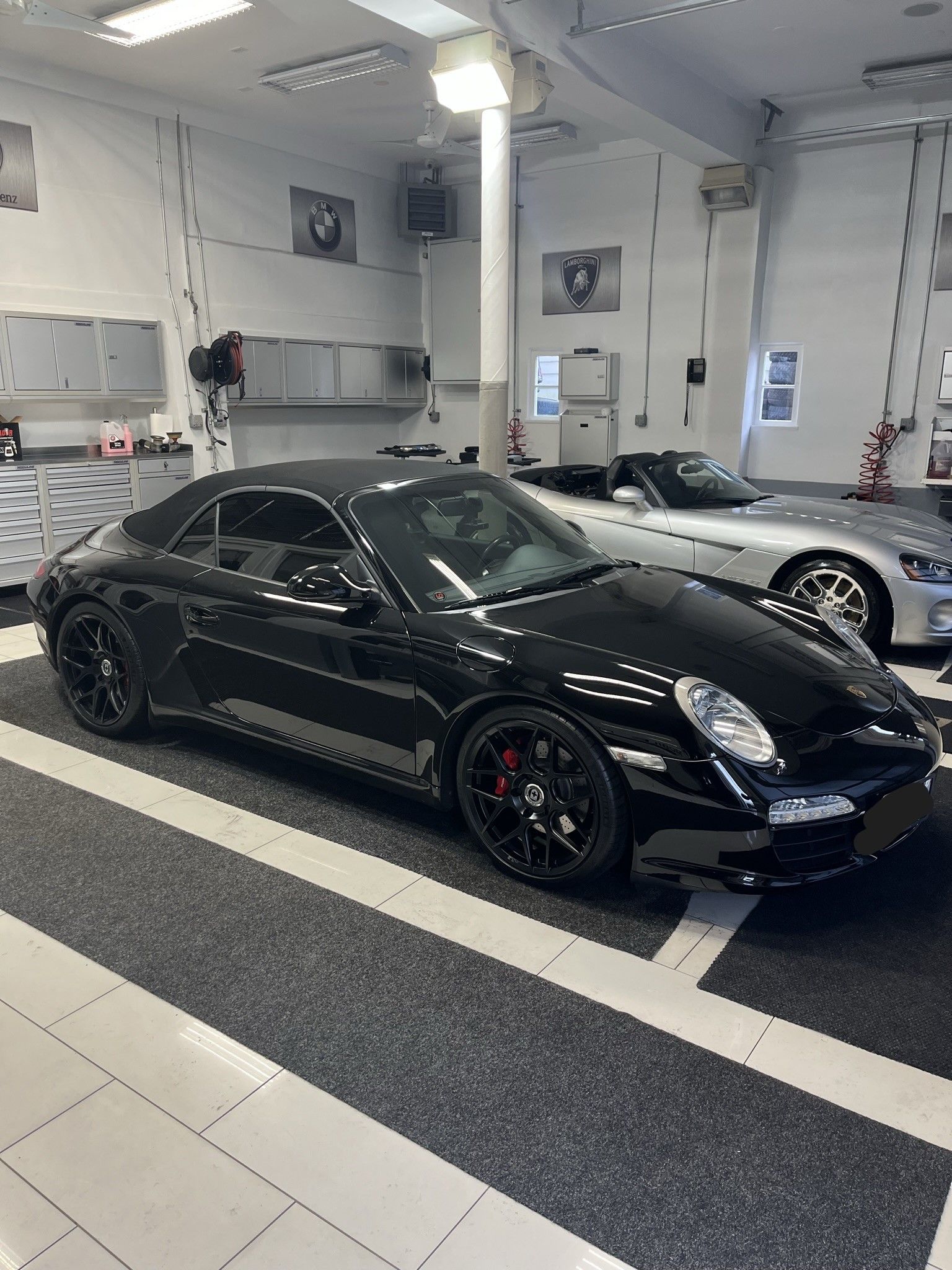 A black porsche 911 cabriolet is parked in a garage.