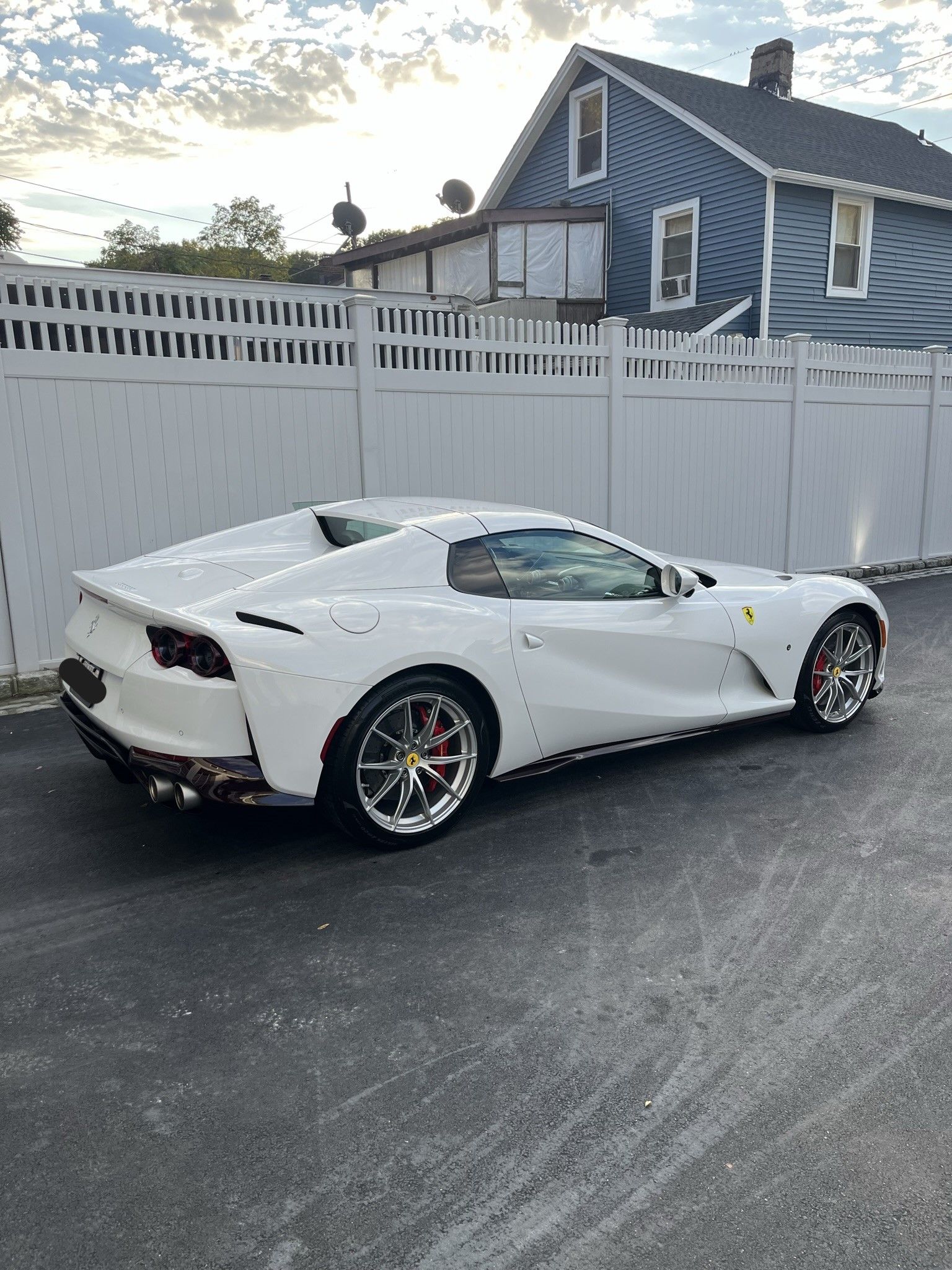 A white sports car is parked in front of a blue house.