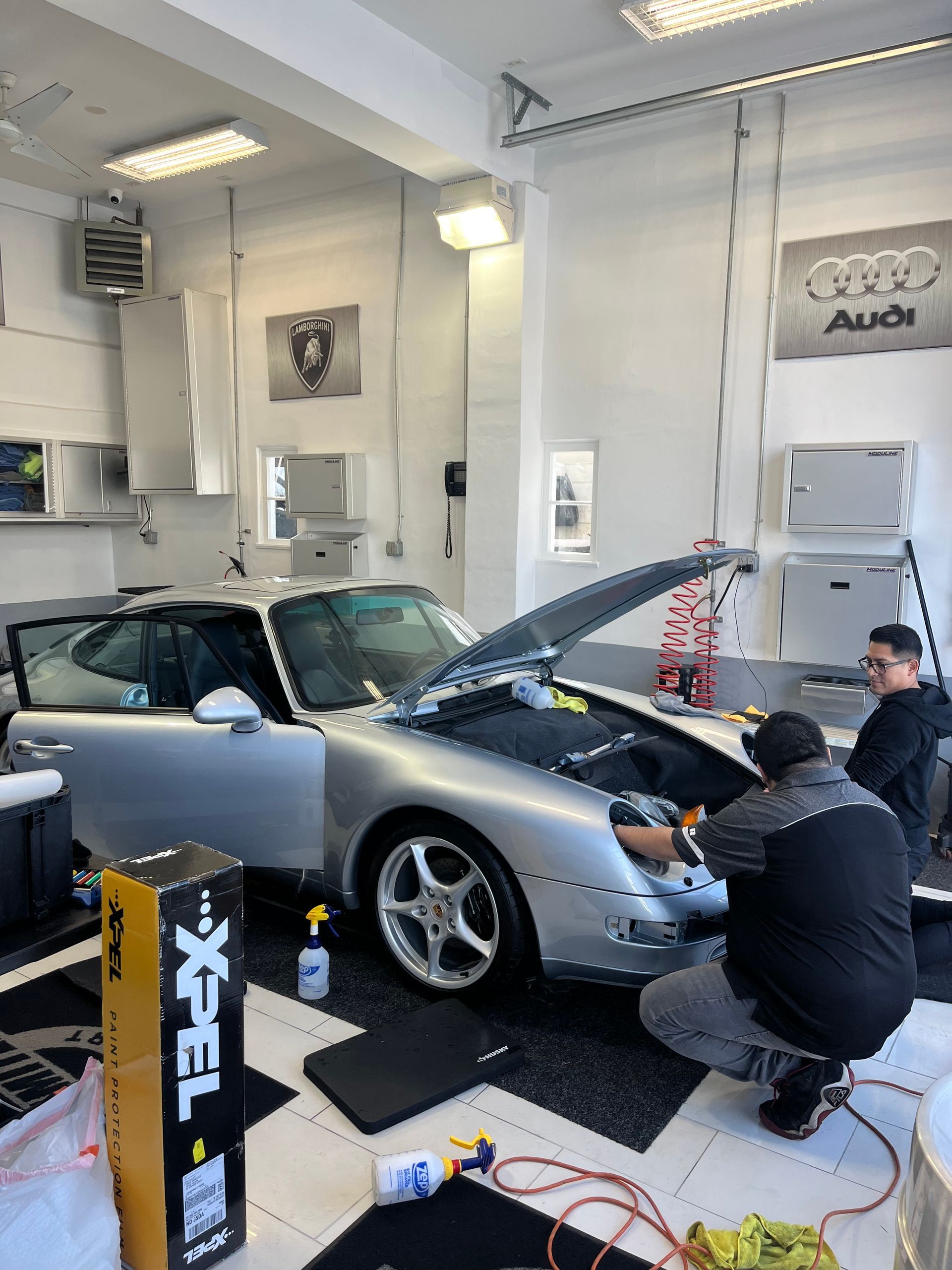 two men are working on a silver car in a garage .