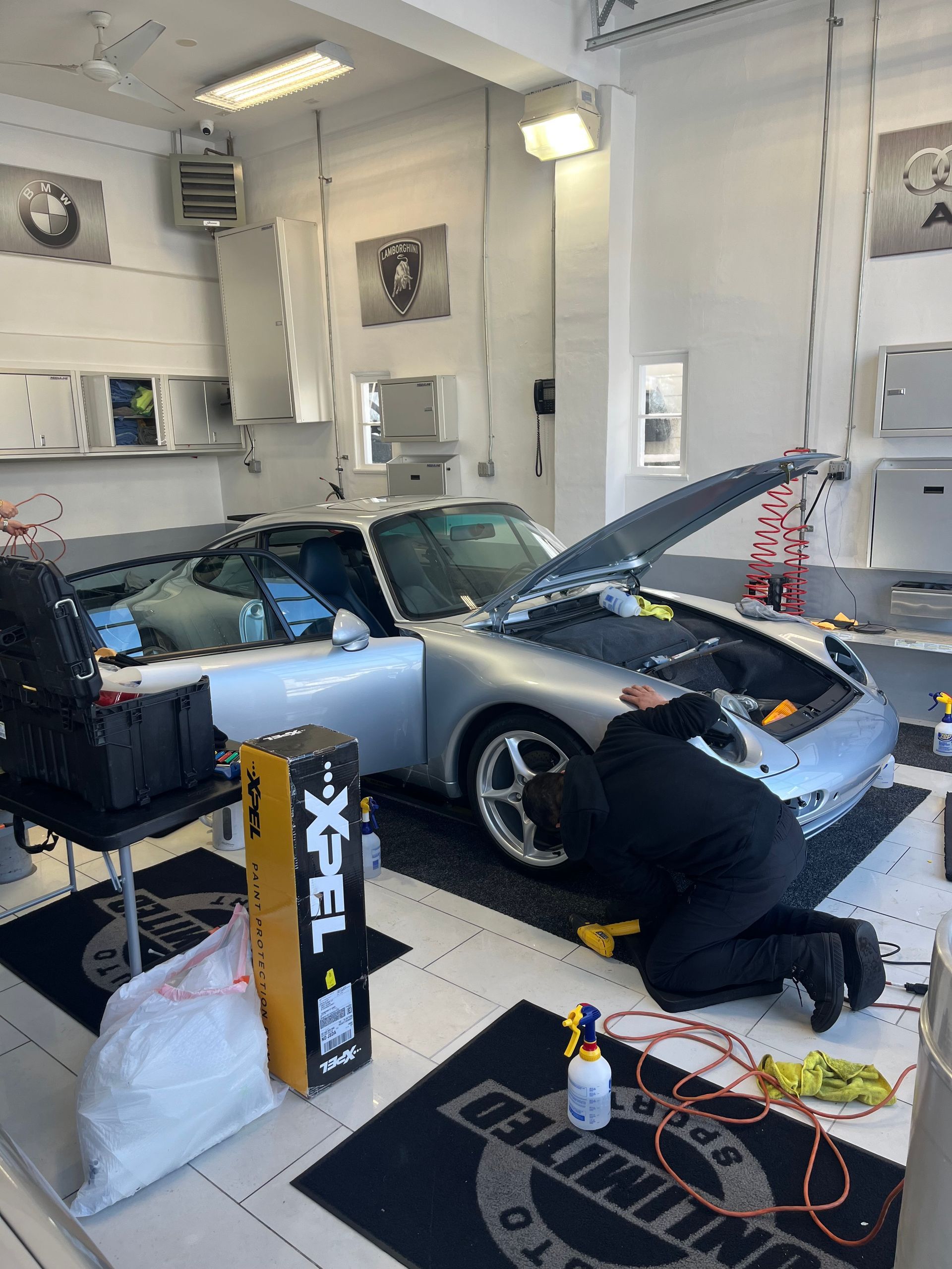 a man is working on a car in a garage with the hood up .