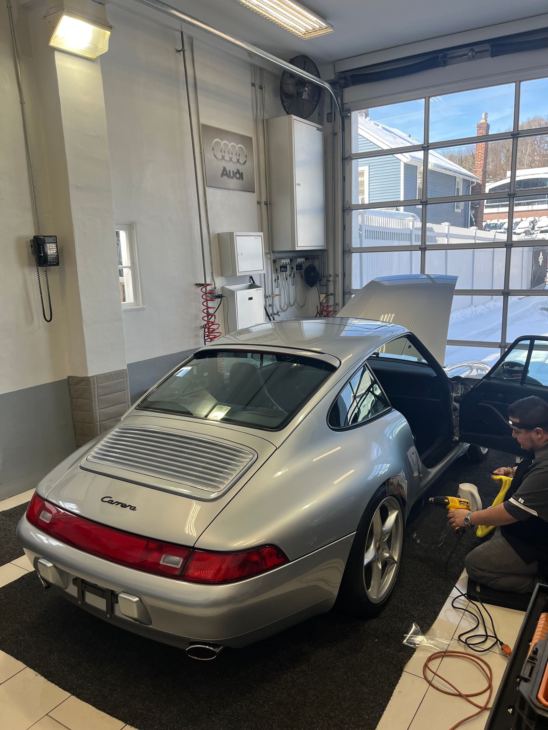 a man is working on a silver porsche in a garage .