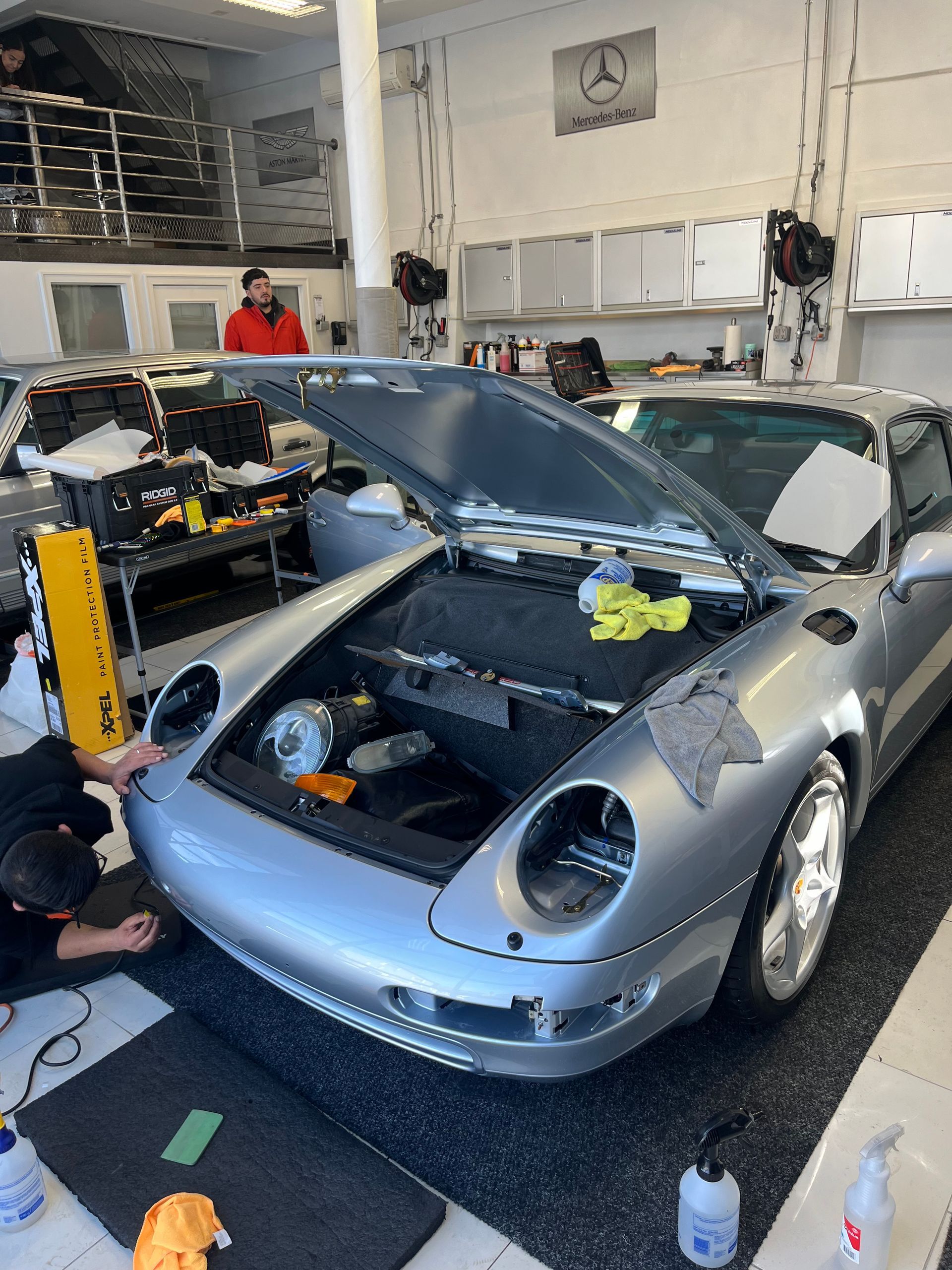 a silver car is being worked on in a garage with the hood open .