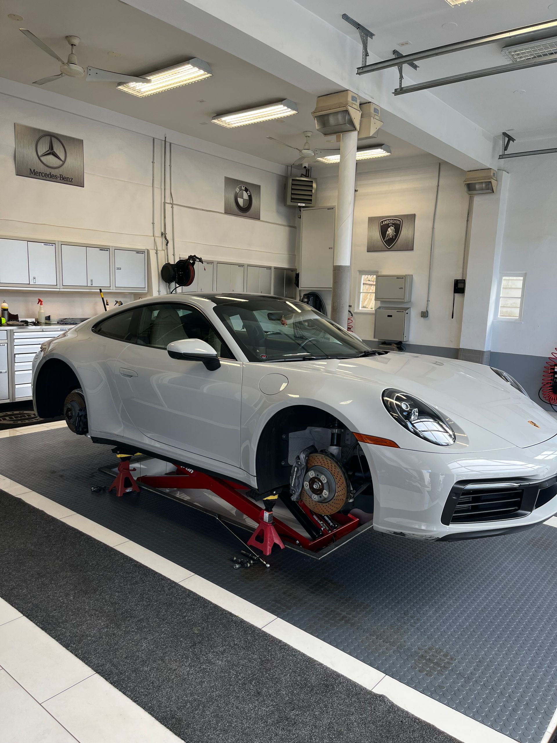 Silver sports car lifted on a red jack in an auto repair shop with white walls and garage equipment