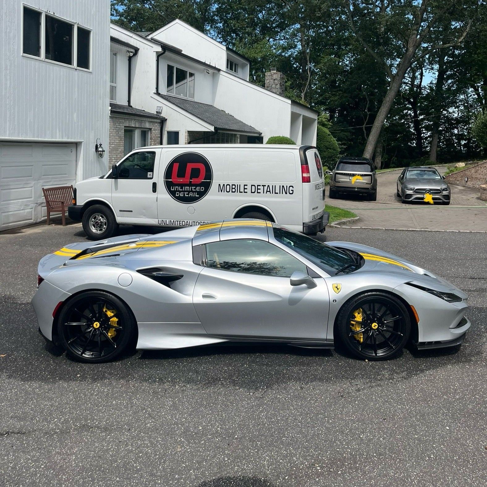 Silver Ferrari in a driveway with black wheels and a white delivery van in the background