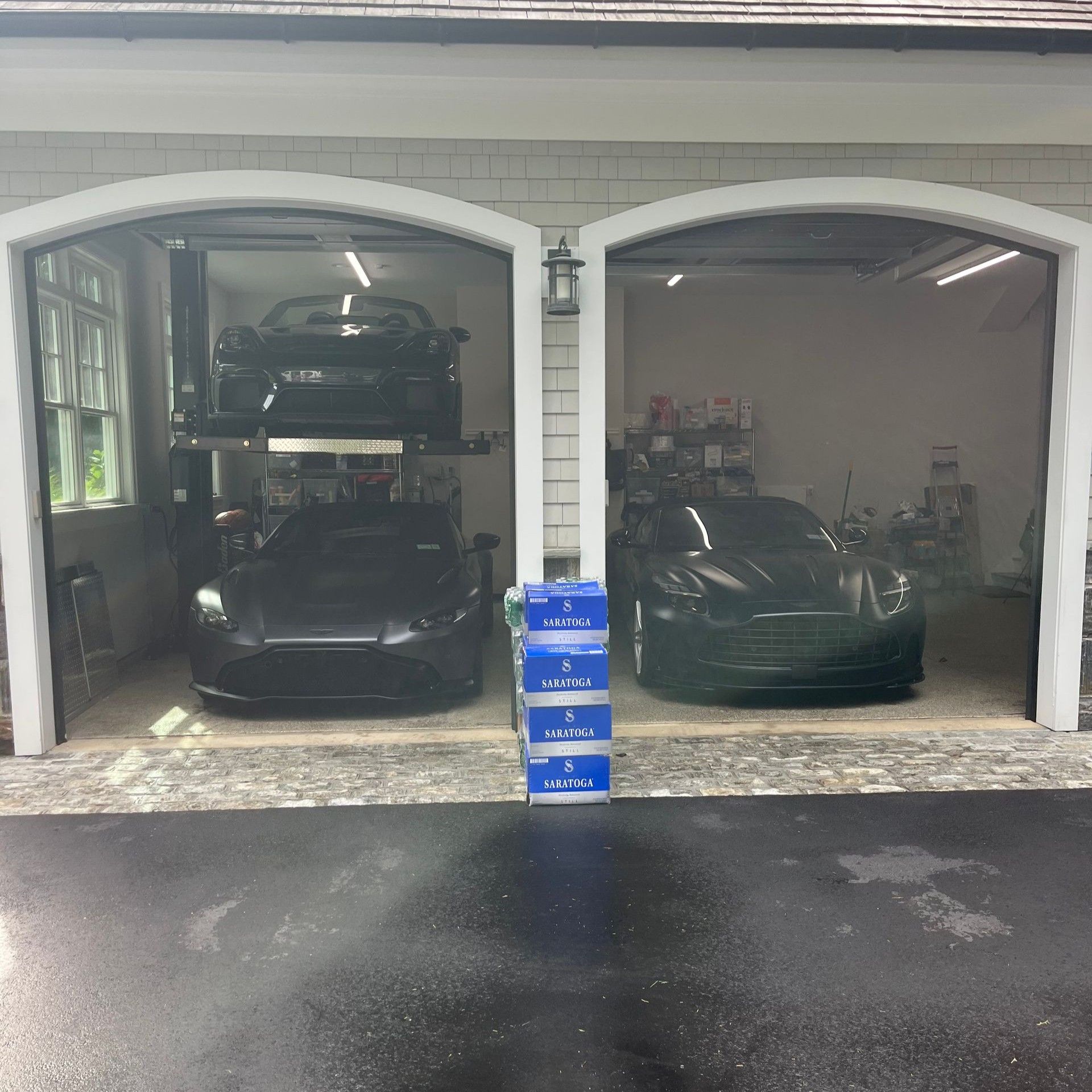 Two cars parked in a garage with open arched doors and a stack of blue boxes in front.