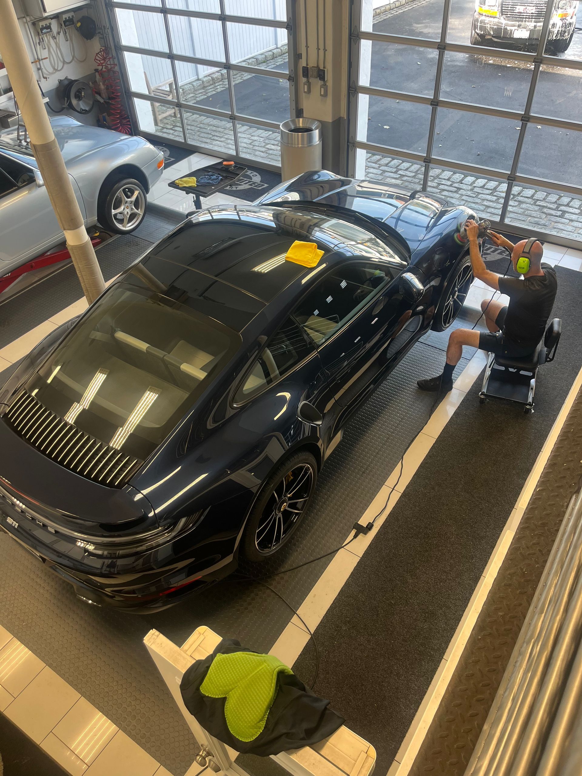 Black car inside a showroom, with a person working beside it and a cloth on the floor.
