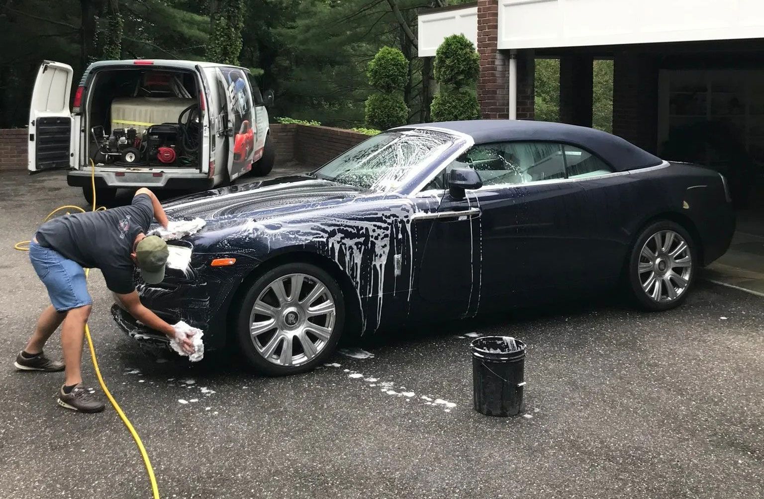 A man is washing a convertible car in a driveway.