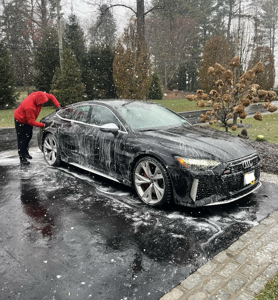 A man is washing a car in the rain.