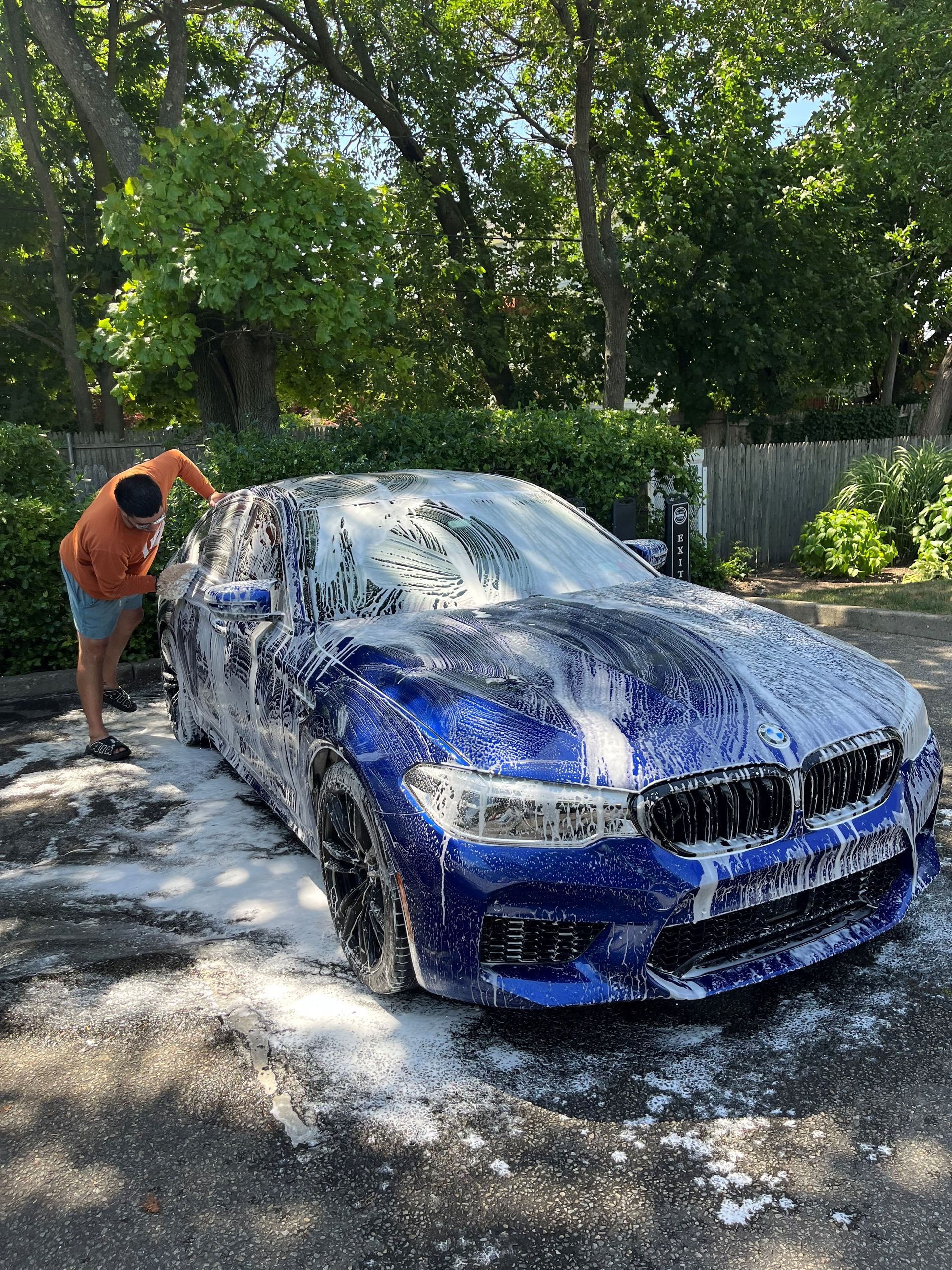 A man is washing a blue car with foam.