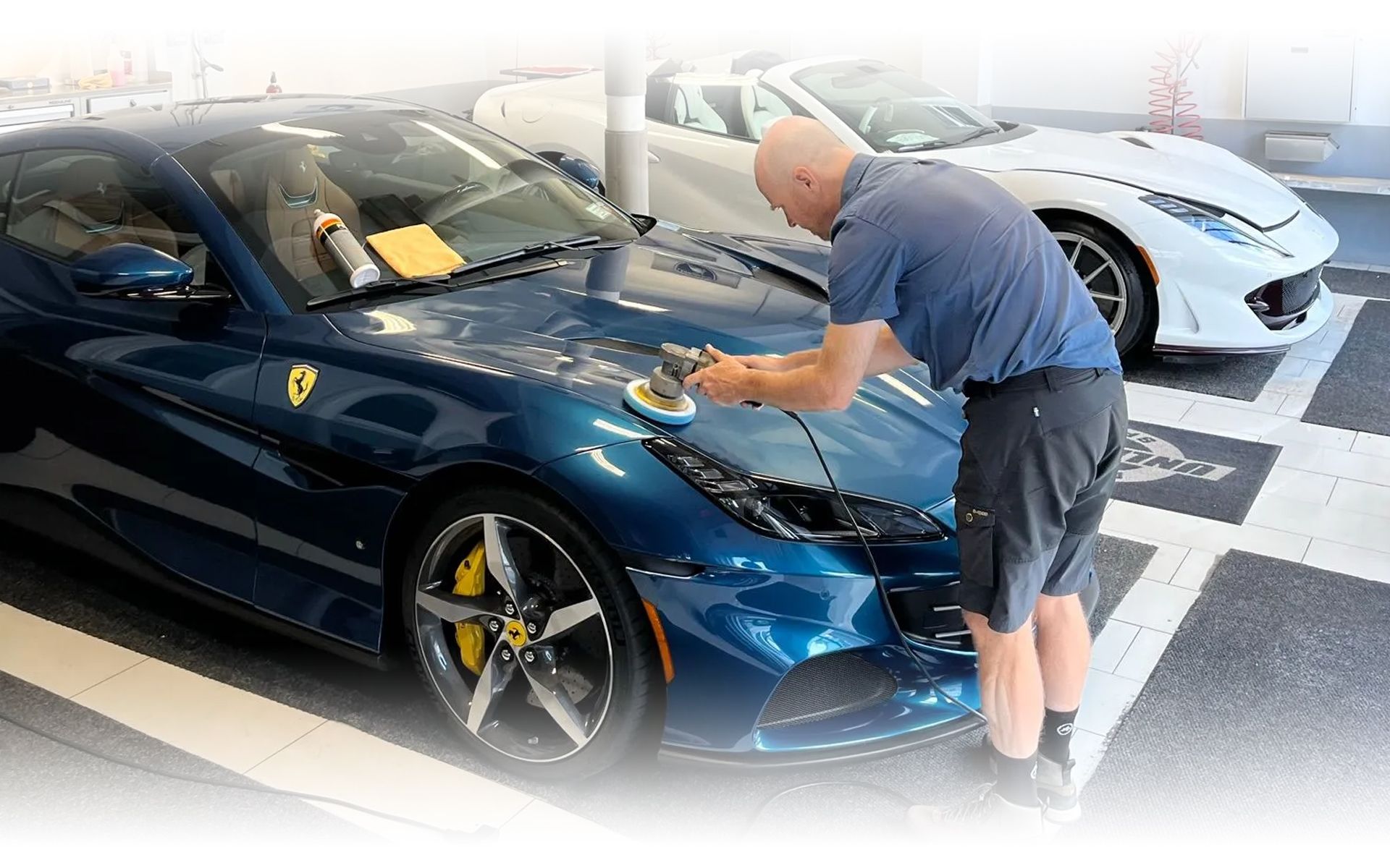 A man is polishing a blue sports car in a garage.