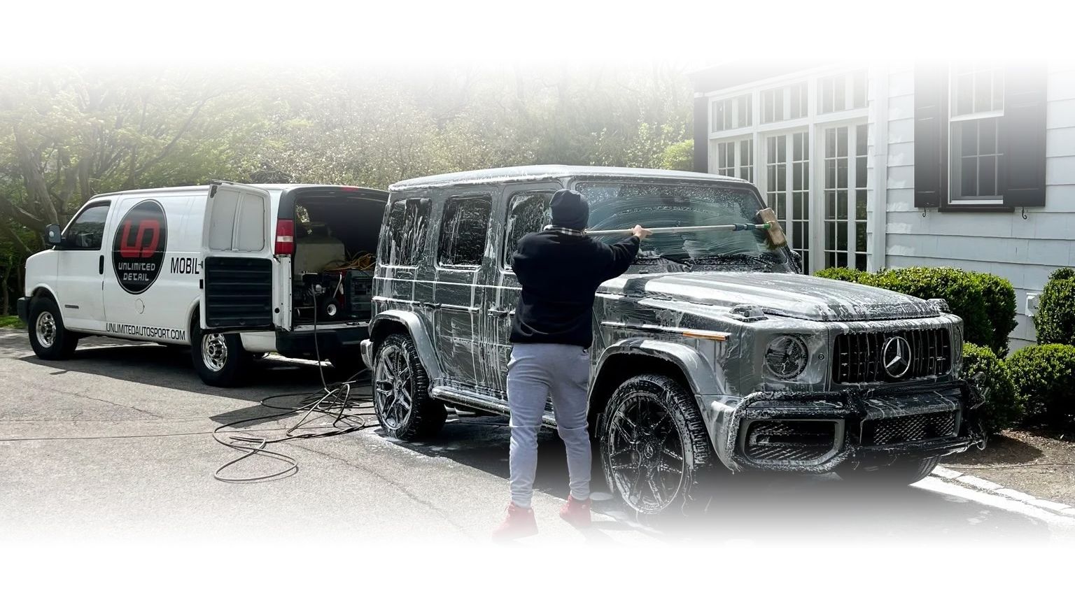 A man is washing a jeep in front of a van.