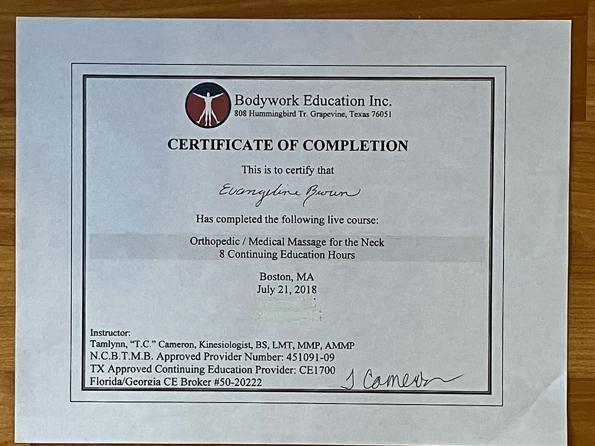 Framed certificate of completion with black text and logo on white paper mounted on a wall.