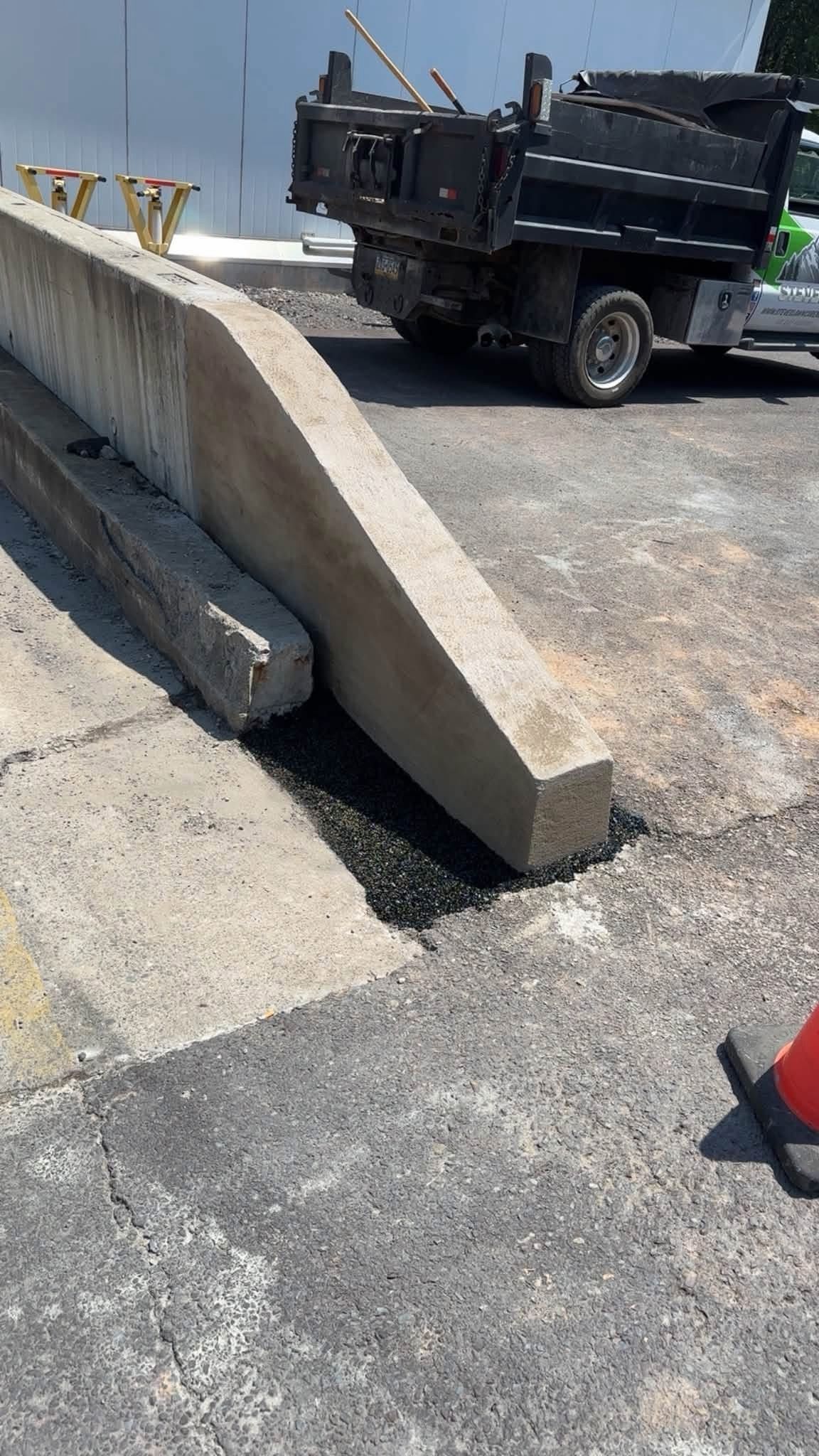 Concrete barrier blocking a road beside a black utility truck in a sunny outdoor lot