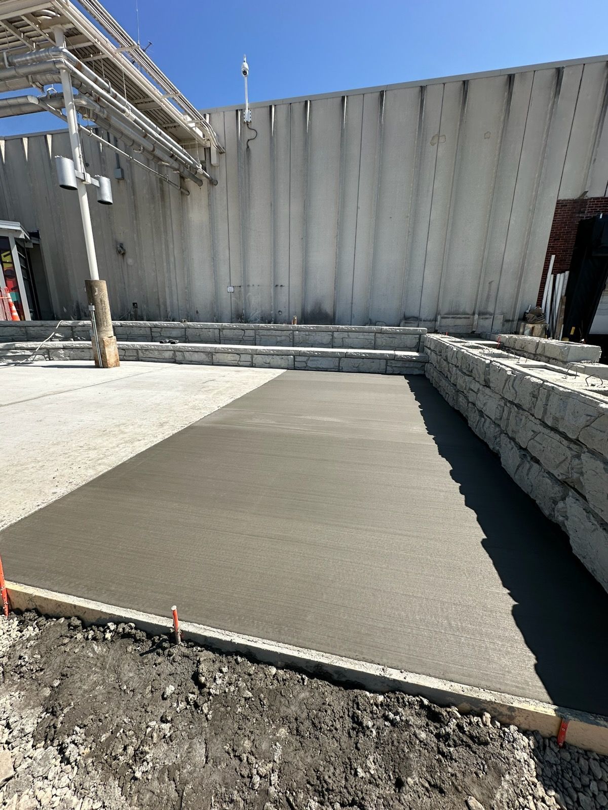 Freshly poured concrete slab at a construction site beside a corrugated metal wall.